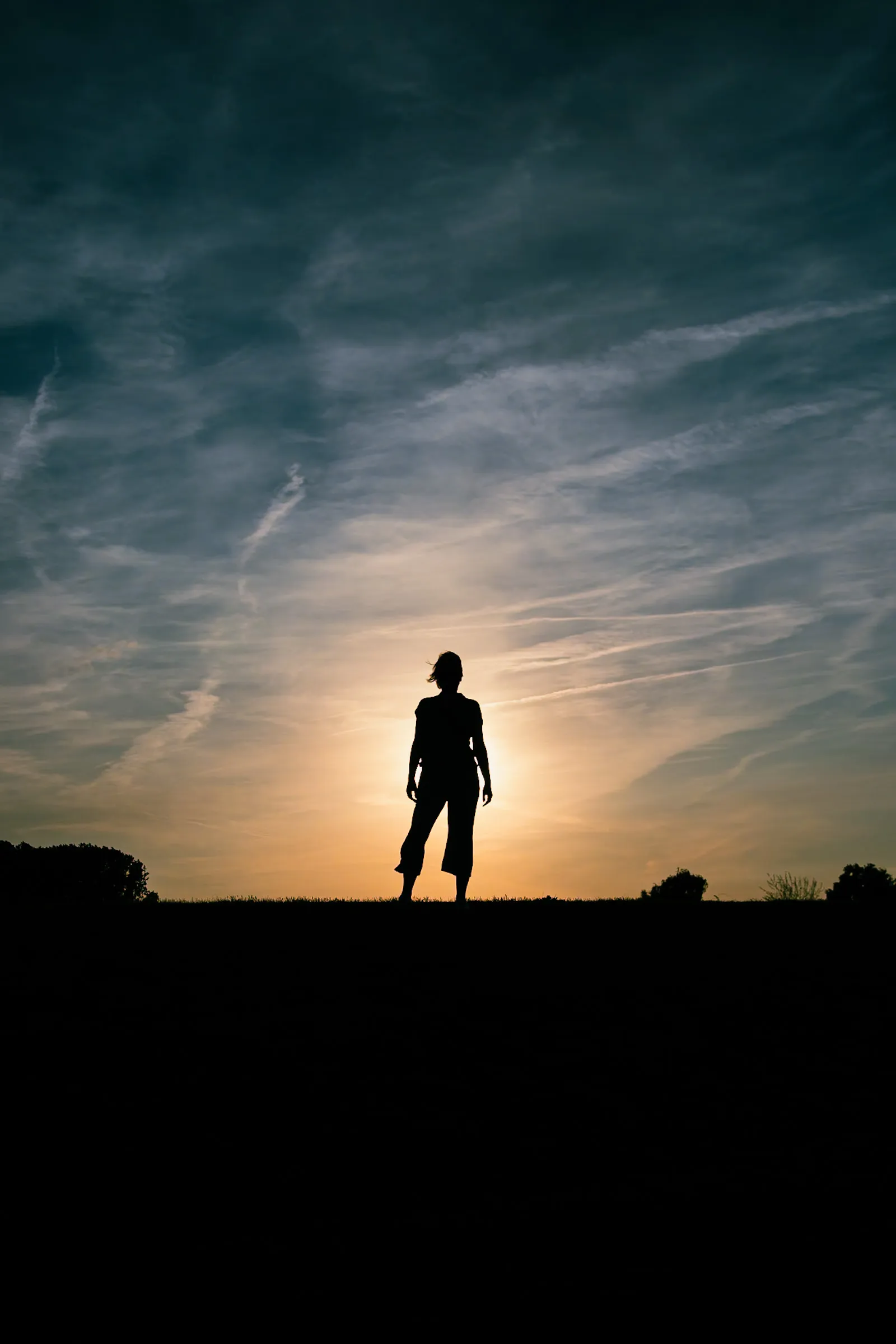 Silhouette of a person standing on a hilltop against a setting sun